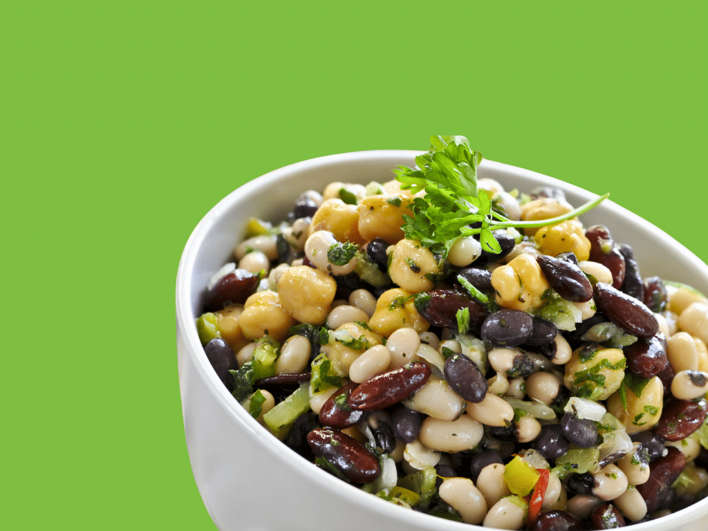 Image of a dense bean salad with various fiber-rich beans topped with fresh herbs on a green background.